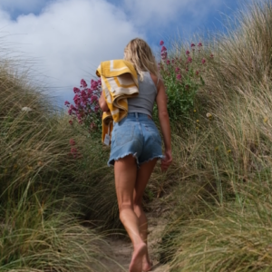 Woman walking within coastal landscape with yellow towel